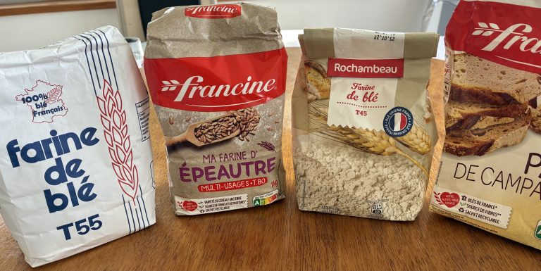 farines t45, t55, t80 et farine d'épeautre alignées et posées sur une table en bois
