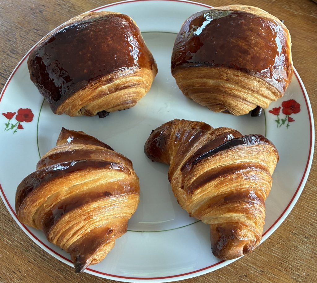 ensemble croissant et pain au chocolat sur une assiette blanche posée sur une table en bois